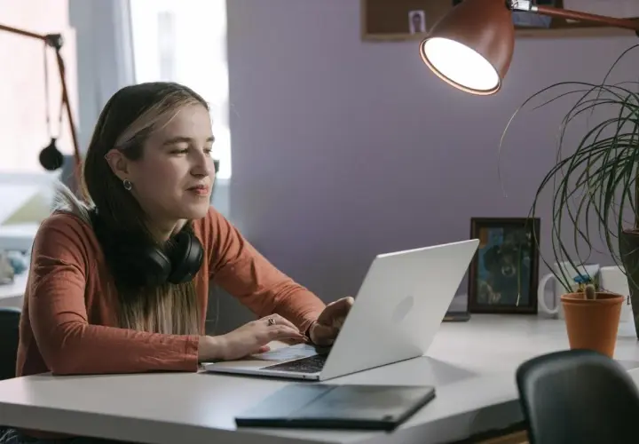 Młoda kobieta z słuchawkami na szyi pracuje na laptopie, być może instaluje aplikację z nieznanych źródeł, ryzykując bezpieczeństwo danych.