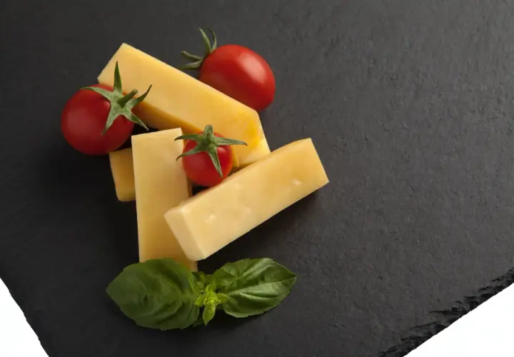 Pecorino co to? Kawałki żółtego sera, pomidorki koktajlowe i listki bazylii na ciemnej desce.