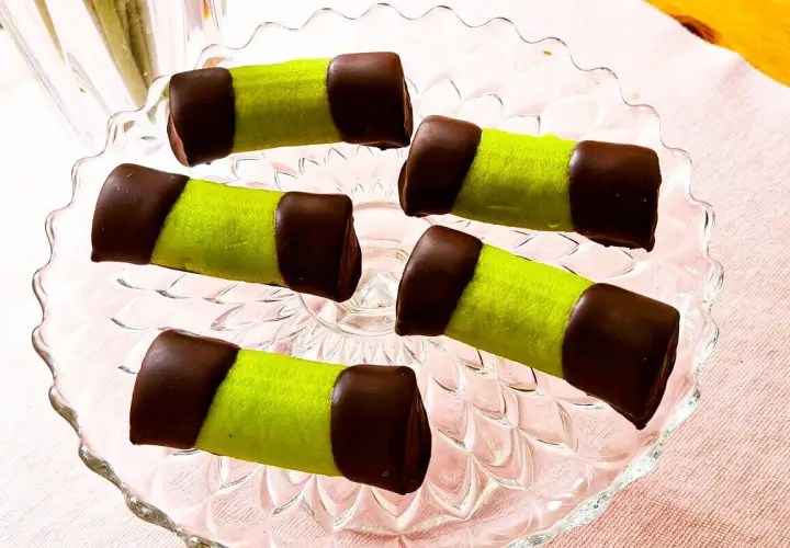 Fem gröna bakelser med chokladtoppar på ett glasfat. Som små dammsugare redo att avnjutas med en kopp kaffe.