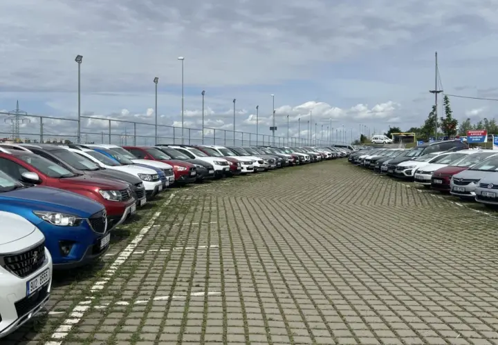 Duży plac z rzędami zaparkowanych samochodów pod zachmurzonym niebem.