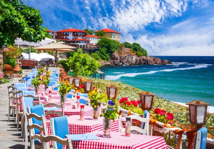 Urokliwa restauracja nad morzem w Bułgarii. Stoliki z czerwono-białymi obrusami i niebieskimi krzesłami czekają na gości, a w tle widać turkusowe morze i malownicze klify.