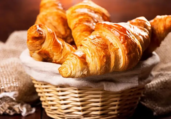 Cesta de mimbre llena de deliciosos croissants caseros, dorados y crujientes, listos para disfrutar.