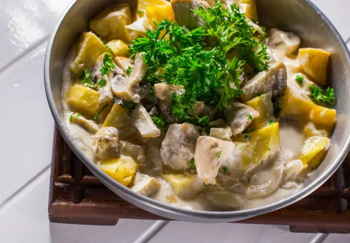 Tradycyjna potrawka z kurczaka z ziemniakami i grzybami w kremowym sosie, udekorowana natką pietruszki.