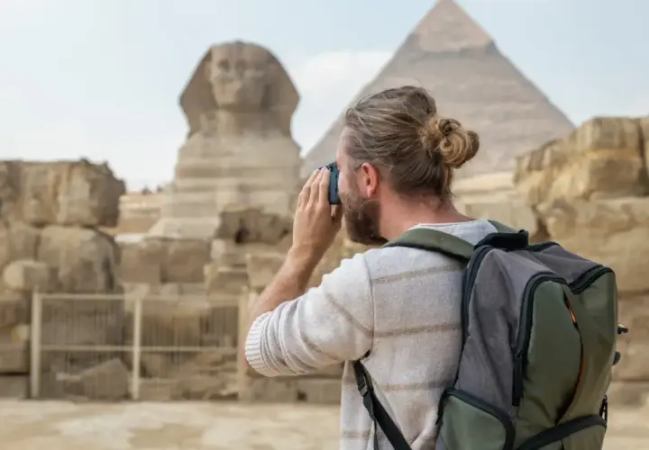 Hombre con mochila y cámara fotográfica admira la Esfinge y las pirámides. Es seguro viajar a Egipto y vivir esta experiencia.