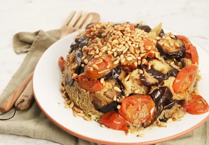 En läcker maklobe kyckling med aubergine, tomater och pinjenötter, serverad på en vit tallrik.
