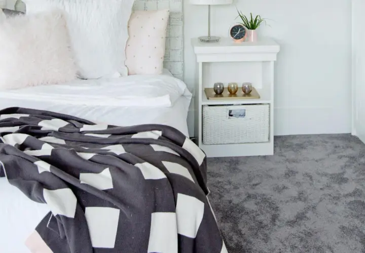 Un letto accogliente con coperta a quadri e un morbido tappeto grigio, perfetto per la posa moquette.