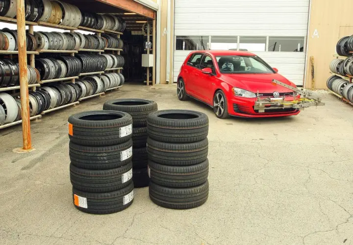 Test opon letnich 225/45 r17. Czerwony VW Golf GTI z zamontowanym sprzętem do pomiarów stoi obok stosów nowych opon.
