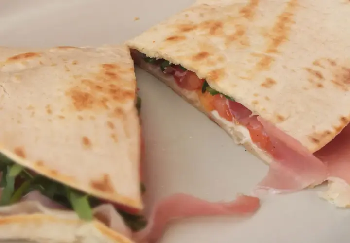 Pyszna piadina romagnola z szynką, pomidorami i rukolą, złożona na pół, gotowa do jedzenia.