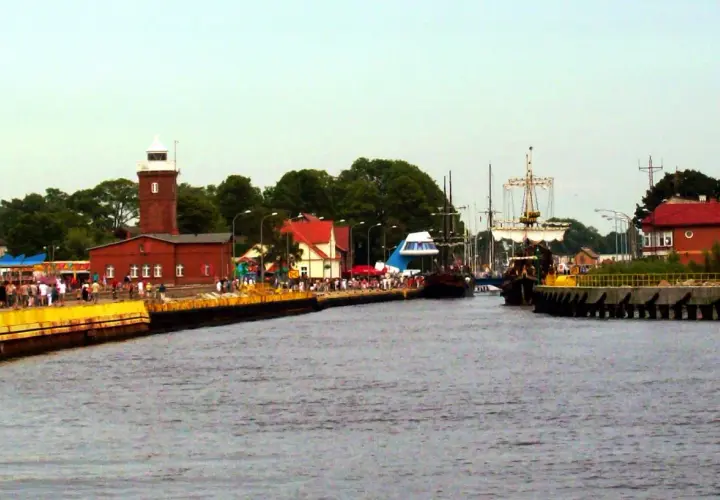 Widok na port z latarnią morską, statkami i ludźmi na nabrzeżu.