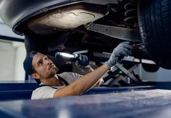 Mechanik z latarką bada podwozie auta. Sprawdza, czy potrzebna jest wymiana wahacza, cena usługi zależy od modelu.