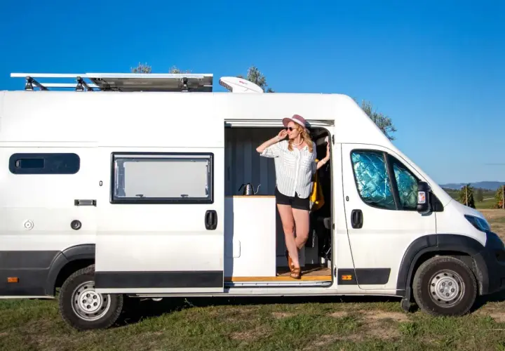 Kobieta w kapeluszu wychodzi z białego kampera z panelem słonecznym na dachu. Jej camper system jest gotowy na przygodę.