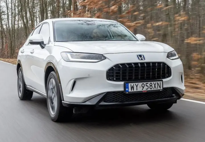 Biała Honda ZR-V przemierza leśną drogę, ukazując swój elegancki design i dynamiczną sylwetkę.