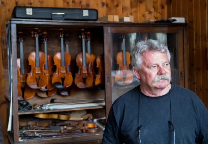 Mistrz lutnik, który robi skrzypce, stoi obok gabloty pełnej instrumentów.