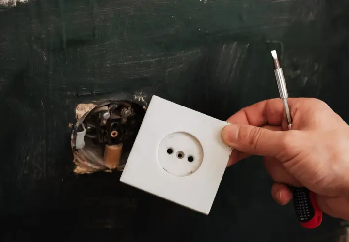 Dłoń trzyma białą ramkę gniazdka elektrycznego, gotową do montażu. To kluczowy element, który działa jak wyzwalacz wzrostowy dla domowej instalacji.