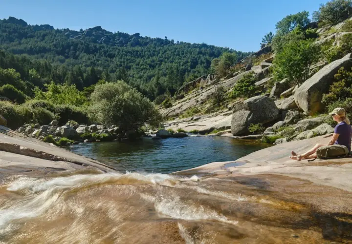 Una mujer descansa junto a unas pozas en Madrid, rodeada de naturaleza y rocas.