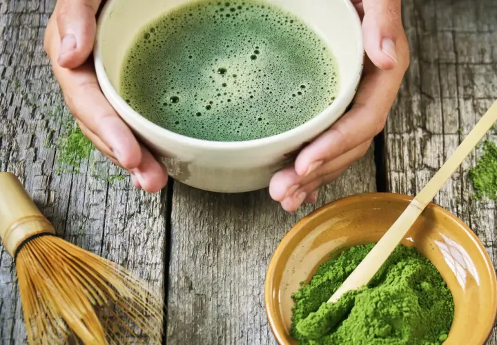 Zielone, spienione napój w miseczce, obok proszek i bambusowa miotełka. Tak przygotowuje się co to matcha.