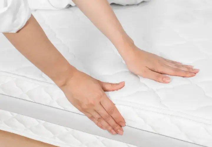 Mains palpant un matelas blanc, peut-être pour évaluer les symptômes d'un matelas trop ferme.
