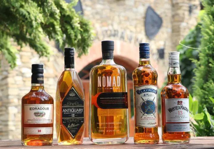 Jak odczytać etykietę szkockiej whisky: Islay, Highlands, Speyside. Pięć butelek whisky na drewnianym stole.