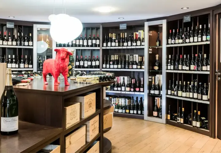 Une cave à vin bien garnie, avec une statue de taureau rouge au centre. Des bouteilles de champagne et de vin sont exposées sur des étagères.