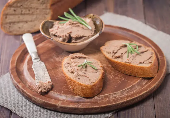 Pyszny pasztet z wątróbki na chrupiących kromkach chleba, udekorowany gałązką rozmarynu. Idealny na śniadanie lub przekąskę.