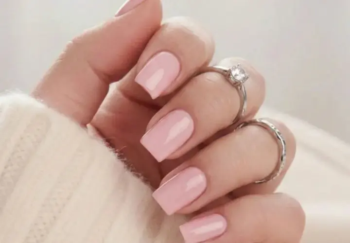 En hand med naglar målade i mjukt nagellack rosa, prydd med två silverringar.