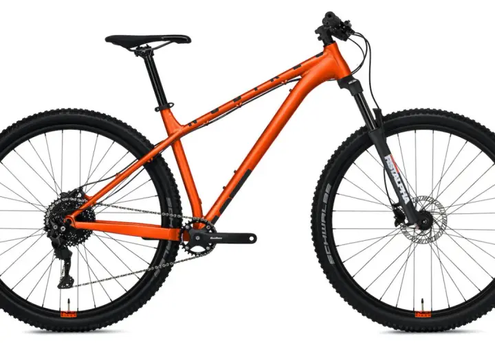 Pomarańczowy rower górski z amortyzatorem z przodu. Czy to hardtail czy full? Ten model to hardtail, idealny na podjazdy i zjazdy.