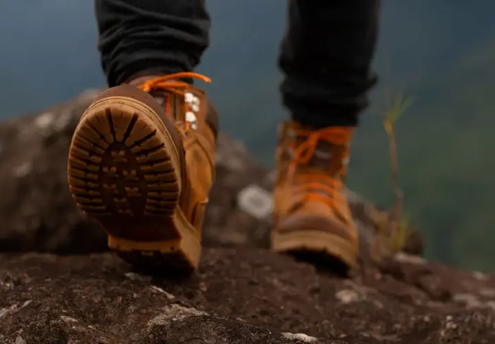 Stopy w brązowych butach trekkingowych z pomarańczowymi sznurówkami stąpają po kamieniach. W butach zastosowano membranę, chroniącą przed wilgocią.