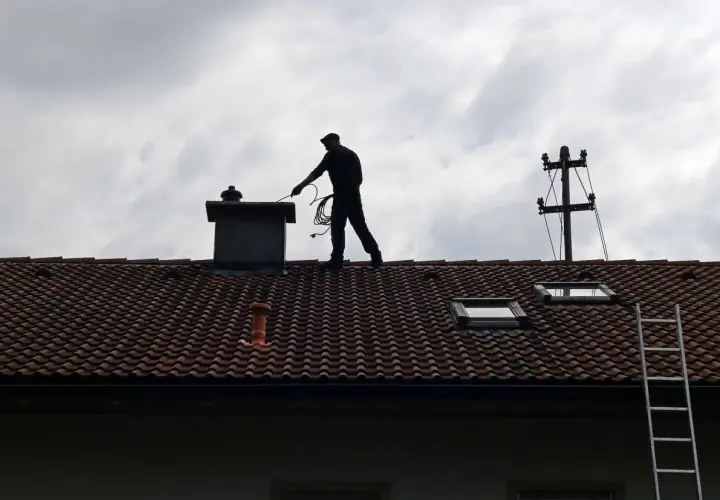 Kominiarz na dachu przygotowuje się do pracy. Zastanawiasz się, ile kosztuje szlamowanie komina?