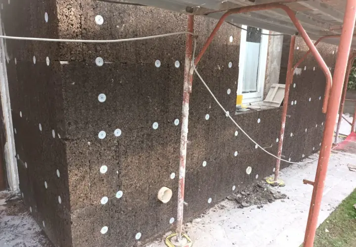 Pannelli di sughero espanso per cappotto termico, fissati con dischi bianchi. Lavori in corso su un edificio.