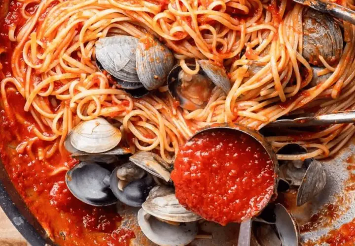 Spaghetti alle vongole, un plat de pâtes aux palourdes et sauce tomate, servi dans une poêle avec une louche de sauce.