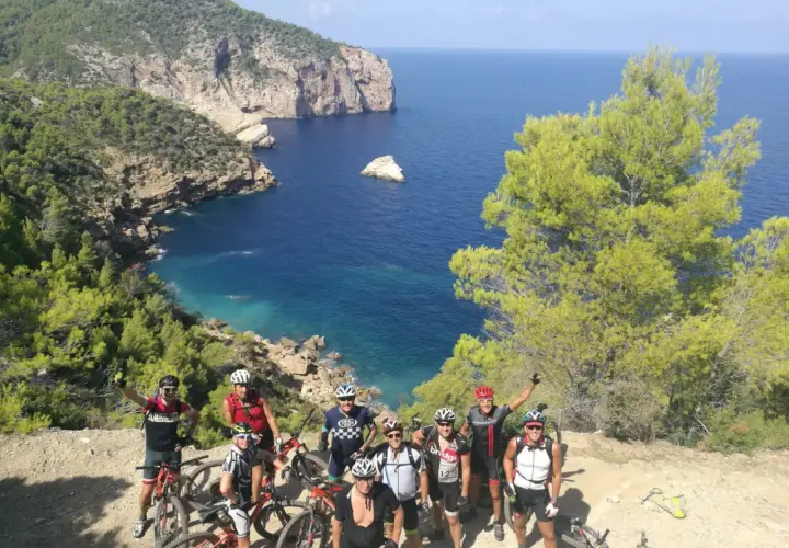 Grupo de ciclistas posa con sus bicicletas en un acantilado con vistas al mar azul. ¡Una aventura en la bicicleta Ibiza!
