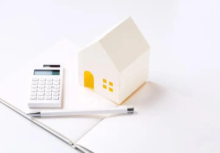 Maison en papier, calculatrice et stylo sur un carnet ouvert, symbolisant les **PTZ travaux soi-même**.