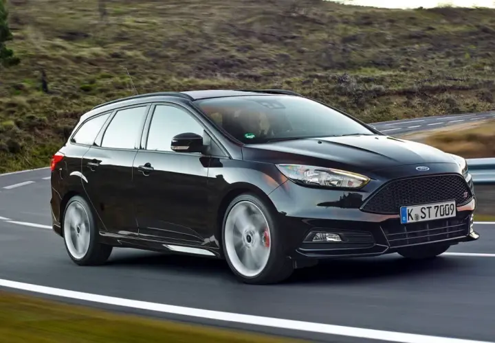 Czarny Ford Focus 3 kombi na zakręcie malowniczej drogi.
