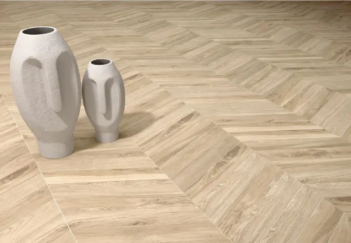 Dwie białe wazony w kształcie twarzy stoją na podłodze z drewnianymi deskami ułożonymi we wzór herringbone.