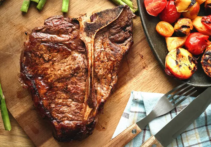 Une côte de bœuf juteuse, accompagnée d'asperges et de tomates grillées, prête à être dégustée.