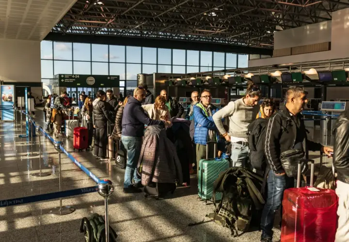 Kolejka pasażerów z bagażami na lotnisku we Włoszech. W tle widać stanowiska odprawy.