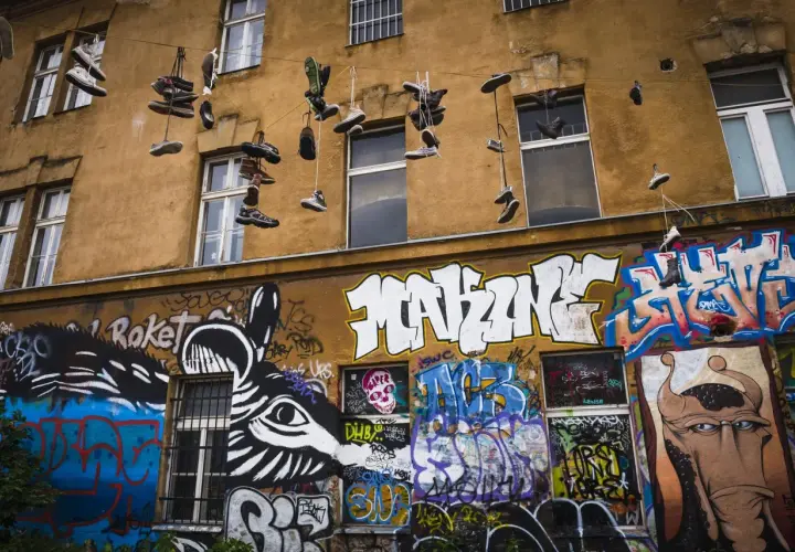 Instalacja artystyczna na fasadzie kamienicy: wiszące buty i kolorowe graffiti.