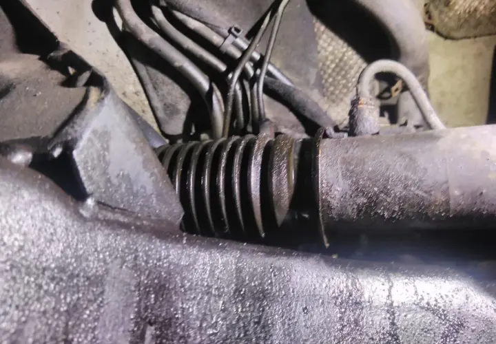 Zbliżenie na skorodowaną maglownicę samochodową z widocznymi przewodami hydraulicznymi.