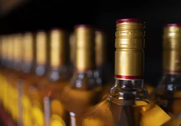 Rząd butelek z alkoholem, złote zakrętki. Zastanawiasz się, ile alkoholu można przewieźć samolotem?