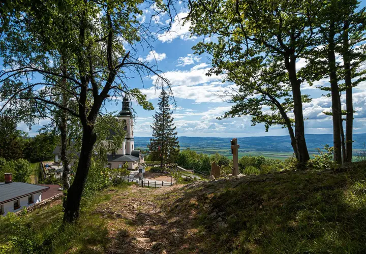 Widok na kościół i krzyż na wzgórzu w **śnieżnicki park krajobrazowy**. W oddali rozciąga się malownicza dolina.