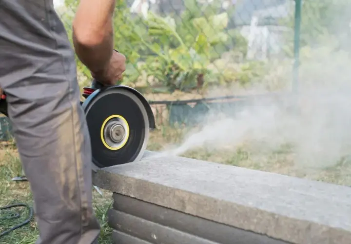 Mann schneidet mit Winkelschleifer eine Betonplatte. Staub wirbelt auf.