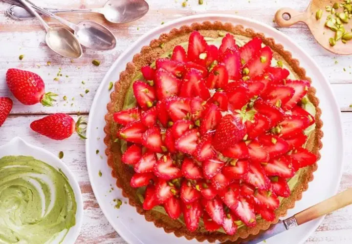 Tarte aux fraises sur pâte brisée, garnie d'une crème verte et de pistaches concassées. Un délice fruité et croquant.