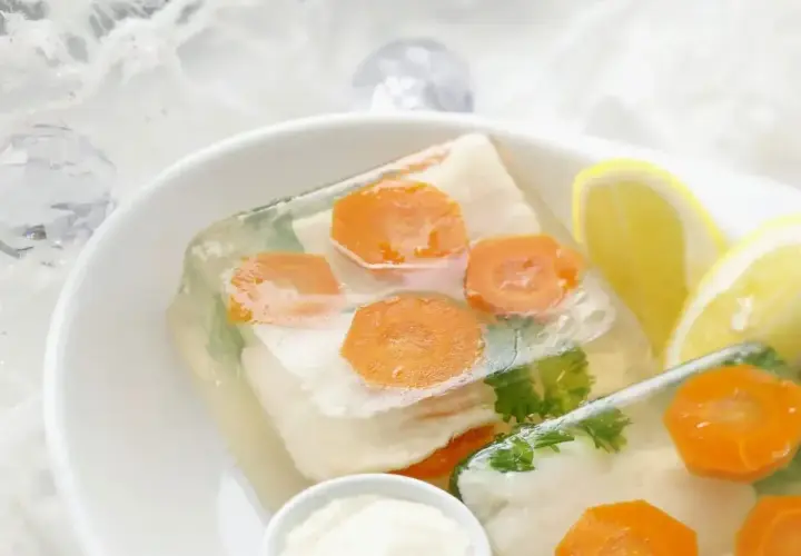 Elegancka ryba w galarecie z marchewką i natką pietruszki, podana z cytryną i chrzanem.