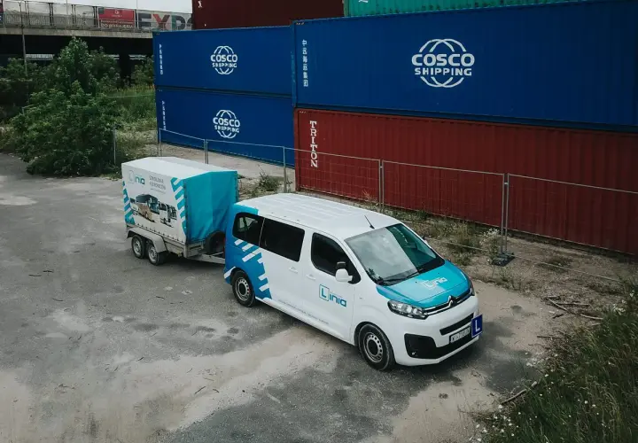 Biały bus z przyczepą, oznakowany logo "Linia", stoi obok kontenerów. To może być szkolenie, gdzie poznasz prawo jazdy b+e koszt.