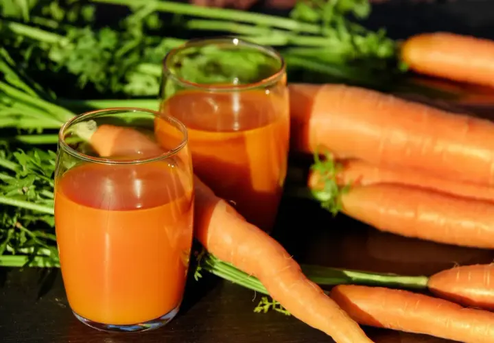 Frischer Karottensaft in Gläsern, umgeben von ganzen Karotten. Ein tolles Beispiel für vitamin a welche lebensmittel.