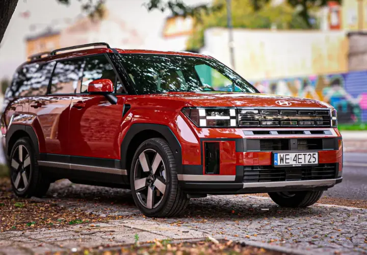 Czerwony Hyundai Santa Fe 2025 z charakterystycznym przednim grillem i światłami, zaparkowany na brukowanej ulicy.