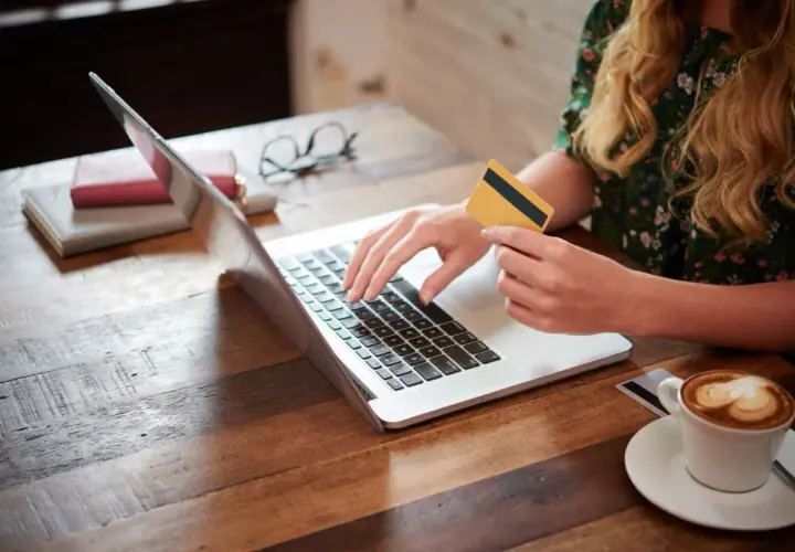 Kobieta z kartą płatniczą na laptopie, szukająca pożyczki dla każdego bez odmowy. Kawa obok.