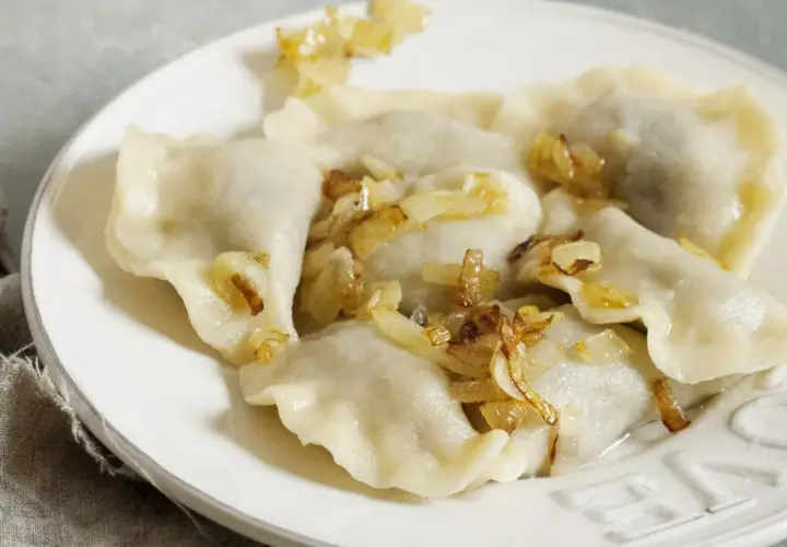 Pyszne pierogi z kapustą i skwarkami, ułożone na białym talerzu, kuszą swoim domowym wyglądem.