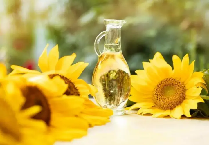 Słonecznikowy olej (helianthus annuus seed oil) w karafce, otoczony przez piękne, żółte słoneczniki.