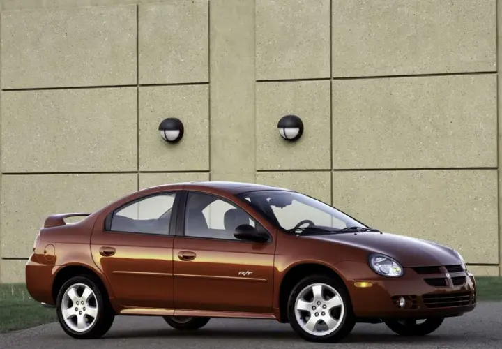 Brązowy Dodge Neon R/T z 2004 roku stoi przed betonową ścianą z dwoma okrągłymi lampami.
